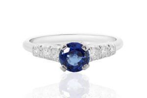 A blue sapphire engagement ring on a reflective background